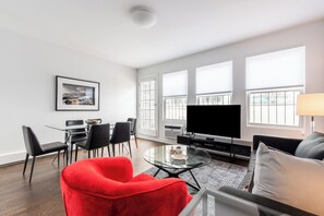 A modern living room with a red chair, a grey sofa, a flat-screen TV, and a dining area with a glass table and chairs.