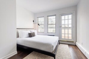 A bedroom with a bed, two windows, a door, and a radiator.