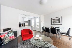 A modern living room with a red sofa, a glass coffee table, and a dining area with black chairs.