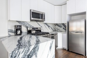 A modern kitchen with a marble island, stainless steel appliances, and white cabinetry.