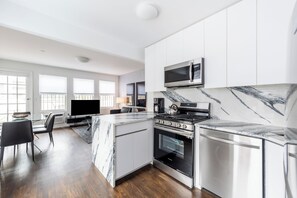 A modern kitchen with white cabinets, a marble countertop, a built-in oven, and a microwave.