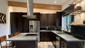 A modern kitchen with dark wood cabinets, stainless steel appliances, and a central island. - The Treehouse Suite with a roof top jacuzzi hot tub. Private and Quiet. (Bonnington Falls)