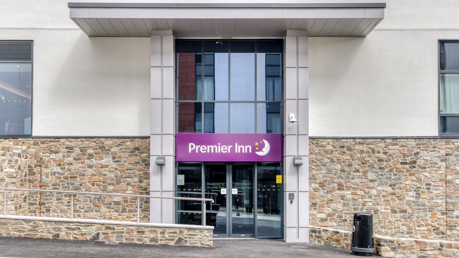 A Premier Inn hotel entrance with a stone facade, a purple sign, and a glass door.