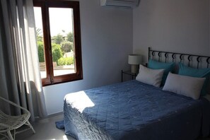 A bedroom with a bed, a nightstand, a lamp, a chair, and a window with curtains.