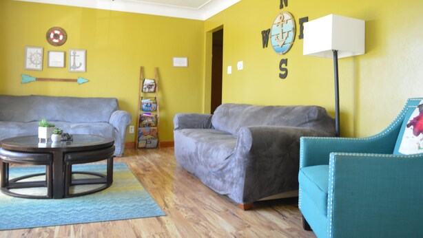 A living room with two grey sofas, a teal armchair, a round coffee table, and a bookshelf. - Reel 'Em Inn (Carlyle)