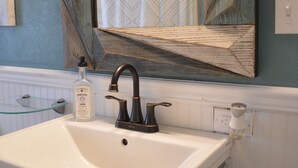 A bathroom with a white sink, a black faucet, and a mirror with a geometric wooden frame. - Reel 'Em Inn (Carlyle)