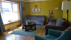 A living room with a blue sofa, a teal armchair, a coffee table with a plant, and a wooden floor. - Reel 'Em Inn (Carlyle)