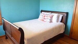A single bed with a wooden frame and white bedding, including a colorful pillow. - Reel 'Em Inn (Carlyle)