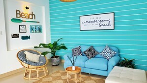 A room with a blue-striped wall, a wicker chair, a blue sofa, and a small table with a plant.