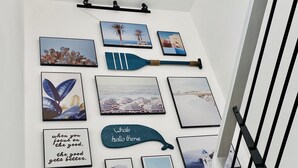 A wall with various framed artworks, including a quote, a whale-shaped pillow, and several nature scenes.