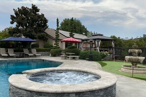 A swimming pool with a hot tub, lounge chairs, and a gazebo.