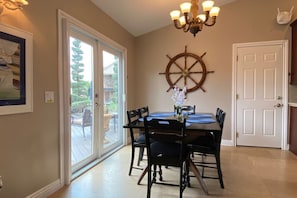 A dining area with a table, chairs, a chandelier, a ship's wheel decoration, and a door.