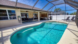 Une piscine couverte avec un espace patio comprenant une table et des chaises, ainsi qu’un coin salon couvert avec des fauteuils.