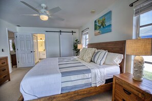 Een slaapkamer met een groot bed, een houten nachtkastje, een plafondventilator en een schilderij aan de muur.