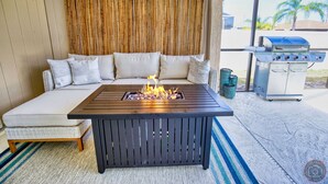 Un espace extérieur accueillant avec un foyer intégré dans une table, un canapé avec des coussins et un barbecue.