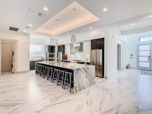 A modern kitchen with a marble island, stainless steel appliances, and a bar area.