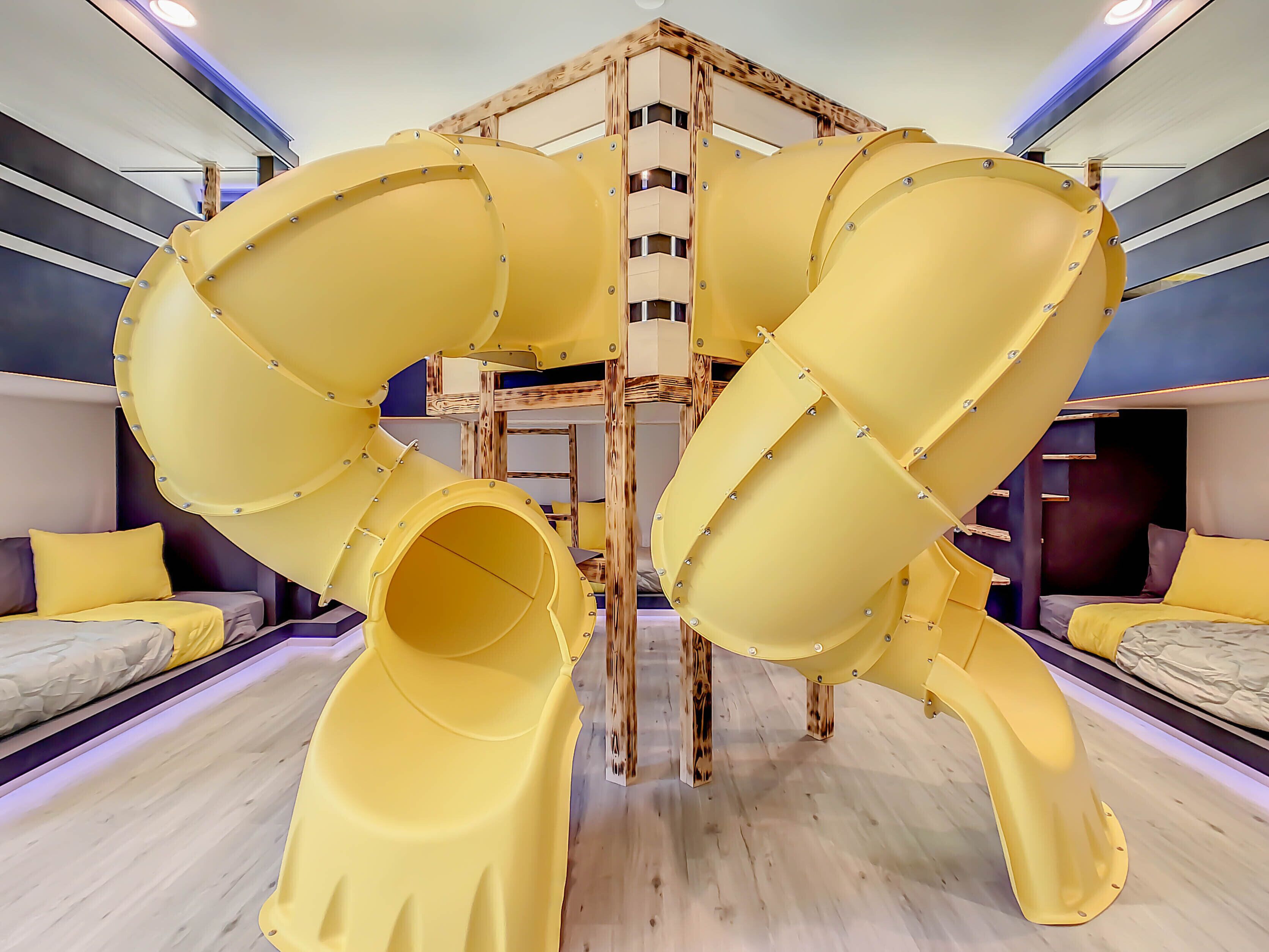 A room with a unique play structure featuring yellow slides and a wooden climbing wall.