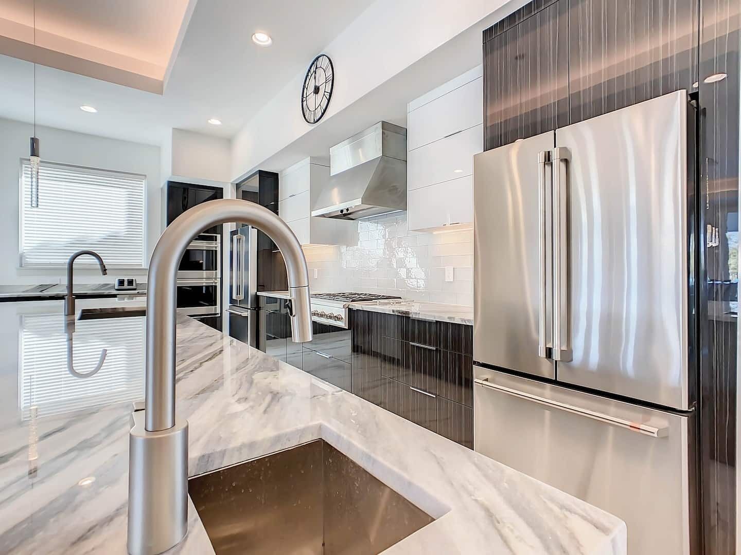 A modern kitchen with stainless steel appliances, a marble countertop, and a large sink.