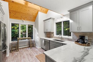 Enjoy a kitchen with a clean design, featuring a wooden ceiling, white cabinetry, and a large window offering a view of the surrounding greenery.