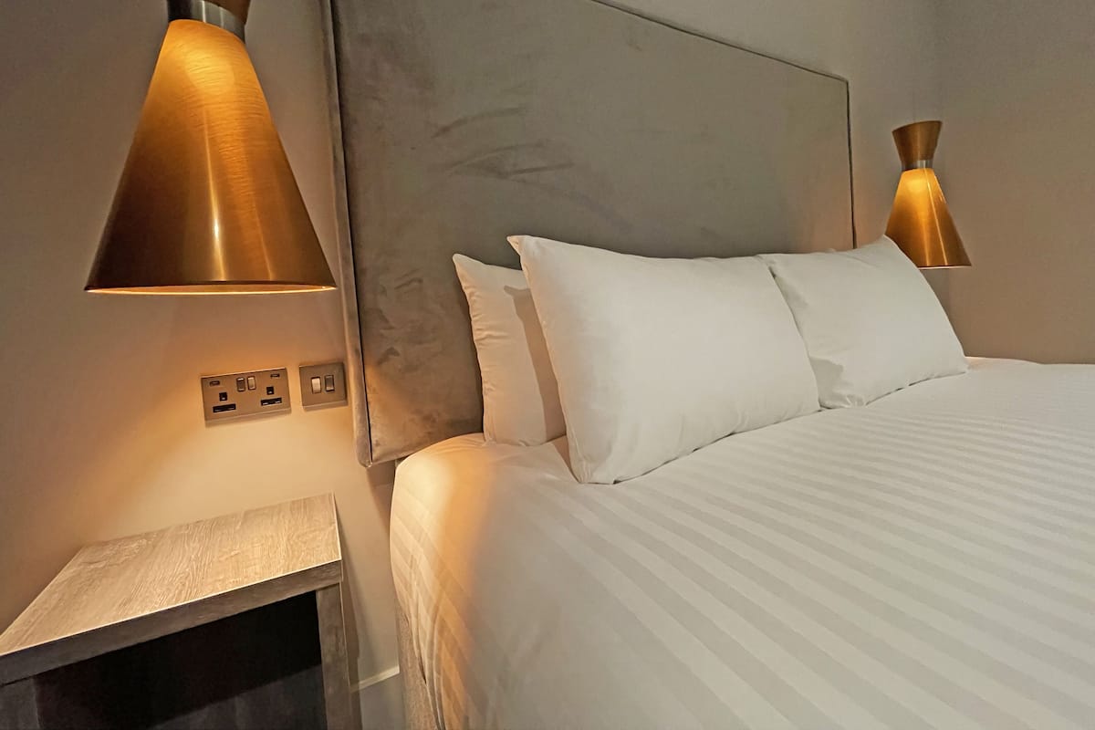 Ein Hotelzimmer mit einem großen Bett, zwei Nachttischlampen, einem Nachttisch und einer an der Wand montierten Bedienkonsole.