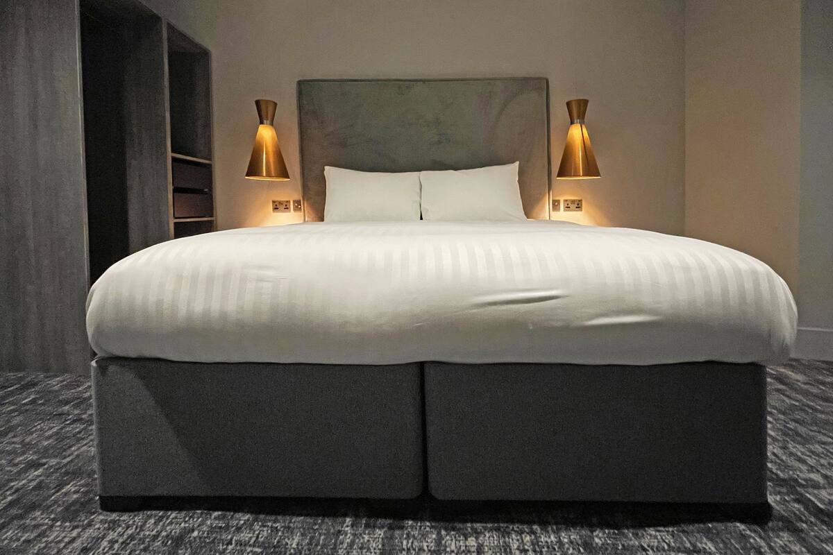 Ein großes Bett mit Kopfteil, zwei Nachttischlampen und Teppichboden.