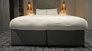 Een groot bed met een grijze hoofdbord, twee bedlampen en een vloerbedekking.