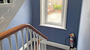 Een trap met witte spijlen en een houten leuning, die leidt naar een kamer met een raam dat uitkijkt op een binnenplaats.