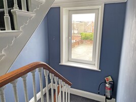 Een trap met witte spijlen en een houten leuning, die leidt naar een kamer met een raam dat uitkijkt op een binnenplaats.