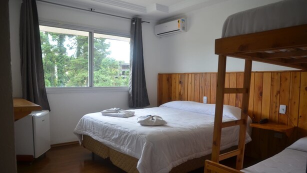 A room with a bunk bed, a single bed, a small table, and a window with curtains. - Pousada Primavera Campos do Jordão (Campos do Jordão)