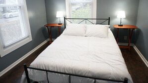 Une chambre à coucher avec un lit, deux tables de chevet avec des lampes et des fenêtres équipées de stores.