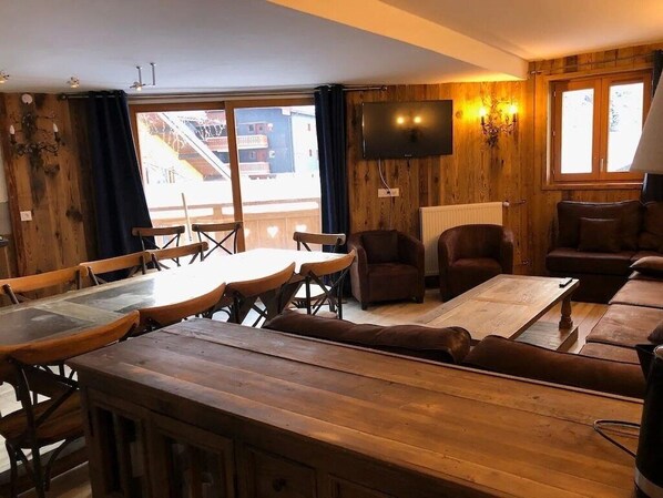 A wooden interior with a dining area, sofas, and a TV mounted on the wall.