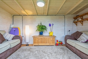 Una habitación acogedora con dos sofás, un aparador de madera, una planta en maceta y una tabla de surf apoyada en la pared.