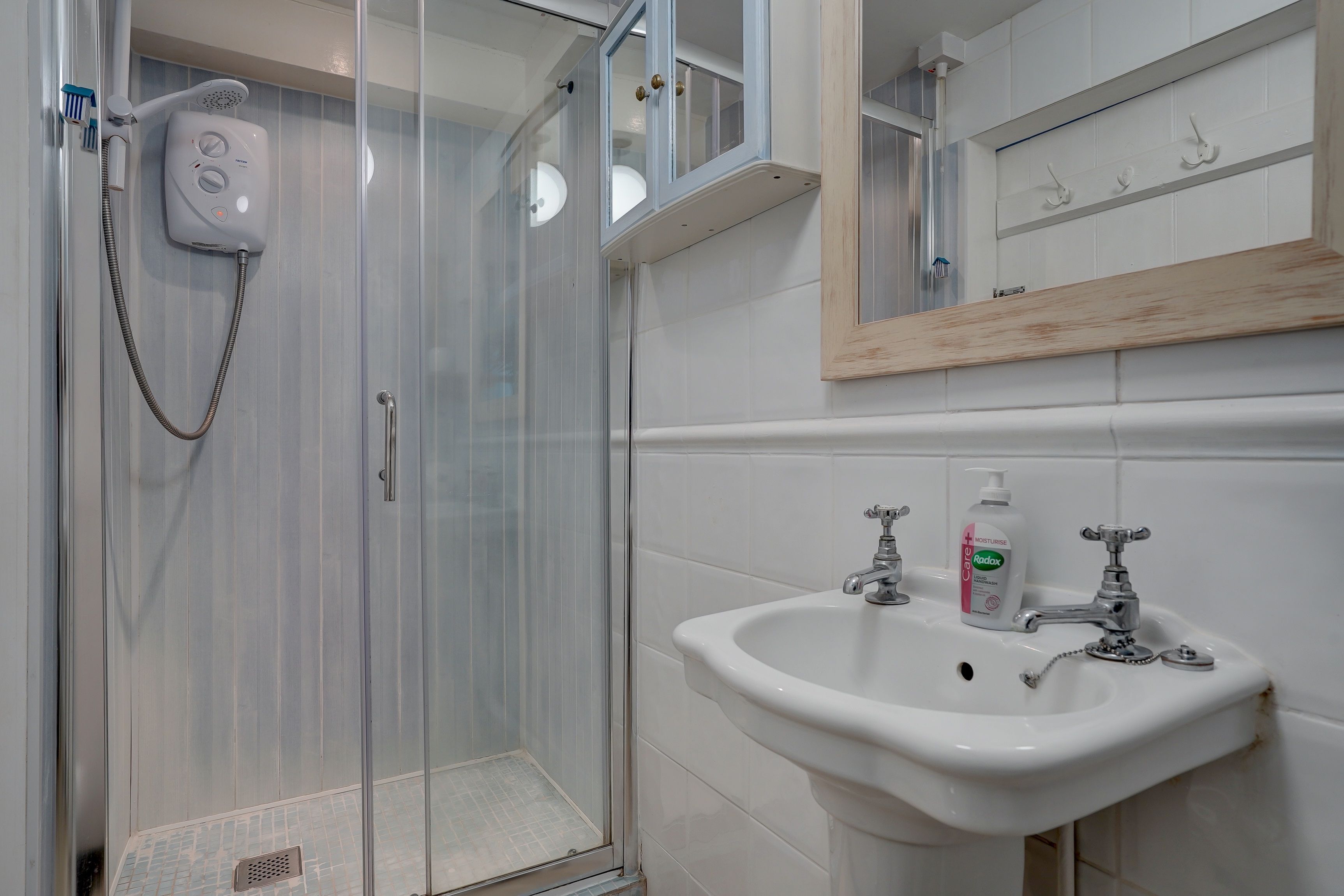 A bathroom with a glass-enclosed shower, a white sink with two faucets, and a mirror above the sink.