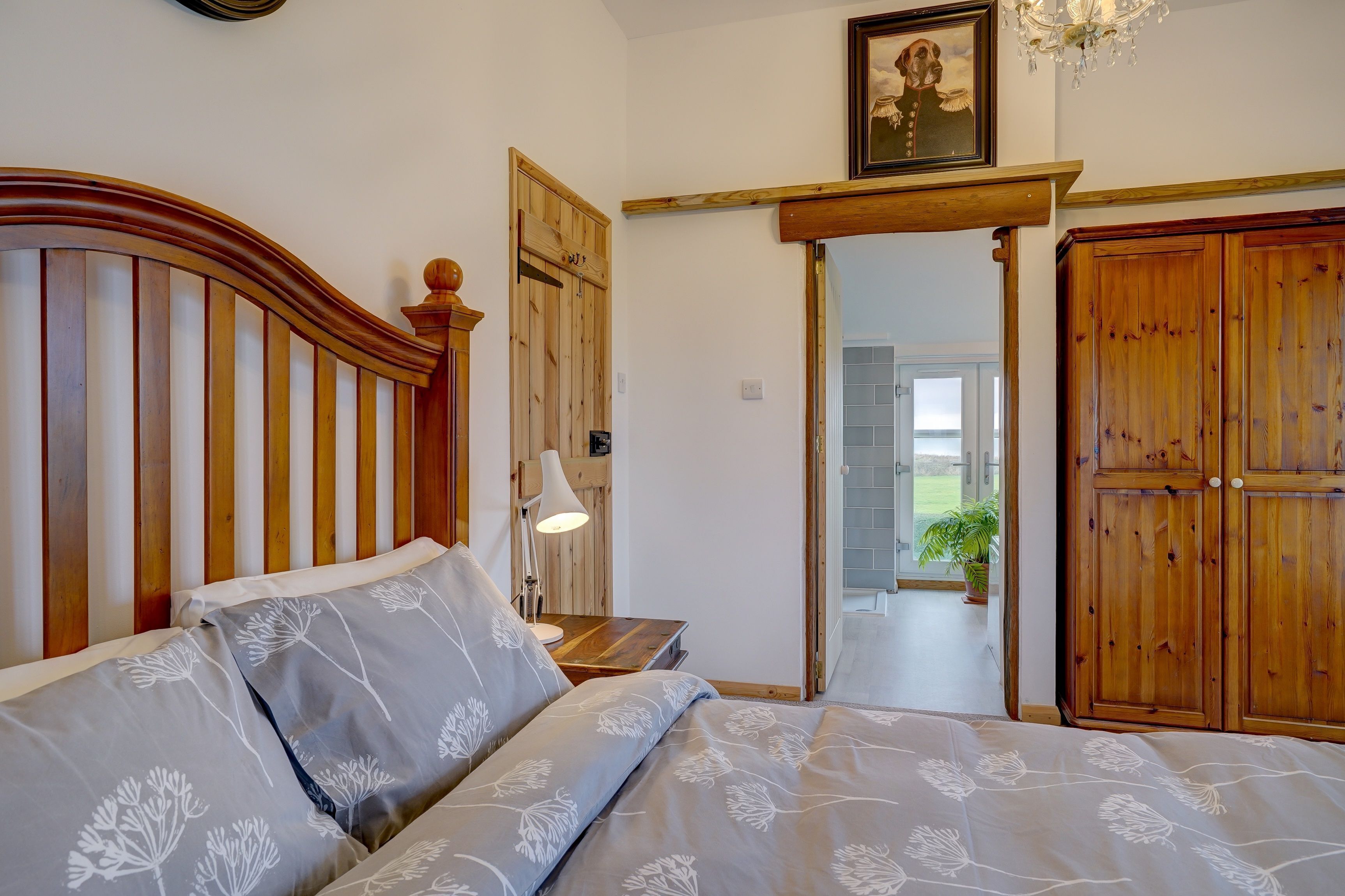 Un dormitorio con cabecera de madera, cama con ropa de cama floral, lámpara de noche y armario de madera.