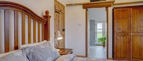 A bedroom with a wooden headboard, a bed with floral bedding, a bedside lamp, and a wooden wardrobe.