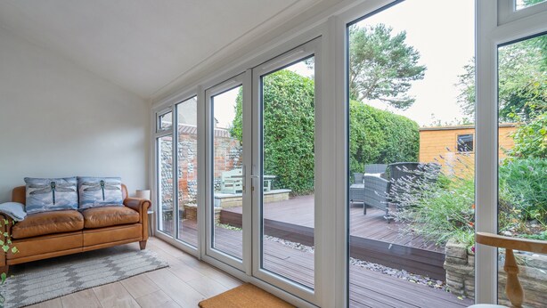 Une pièce avec un canapé en cuir marron, un plancher en bois et de grandes portes vitrées donnant sur une terrasse extérieure.