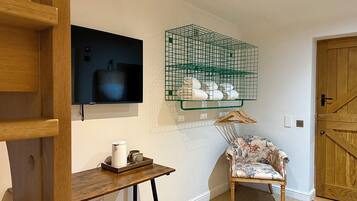 Ein Zimmer mit einem Holzbstuhl, einem kleinen Tisch mit Wasserkocher, einem an der Wand befestigten Fernseher und einem grünen Drahtkorb mit Handtüchern.