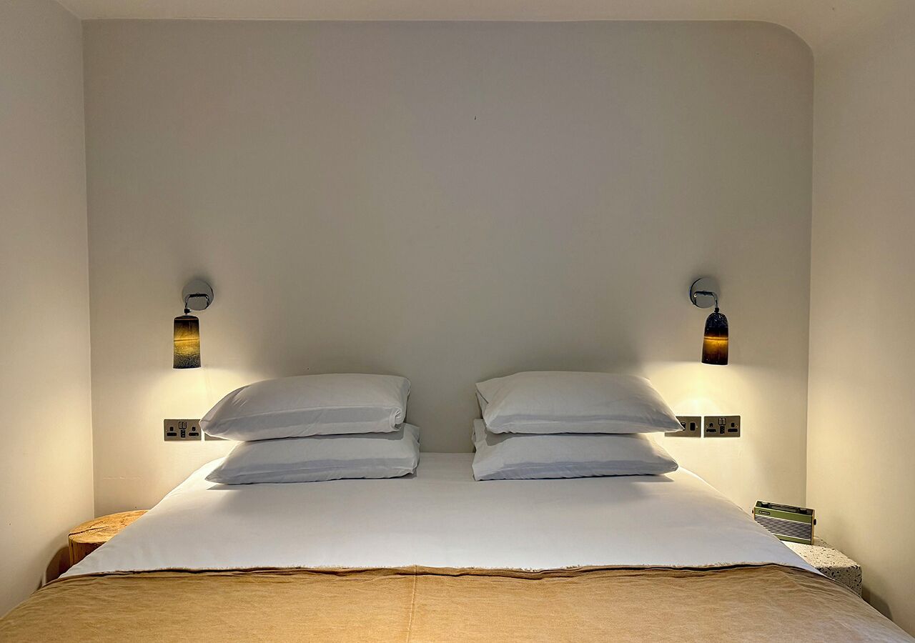 A bed with white linens and two wall-mounted lamps on either side.