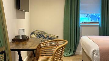Una habitación de hotel con cama, una mesa de comedor con sillas, un televisor montado en la pared y una ventana con cortinas.