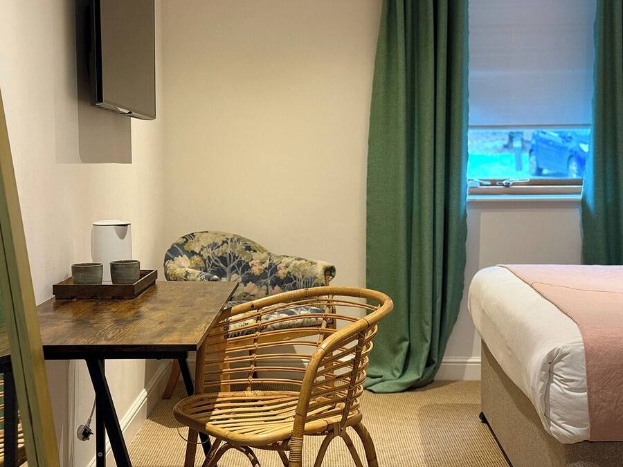 Una habitación de hotel con cama, una mesa de comedor con sillas, un televisor montado en la pared y una ventana con cortinas.