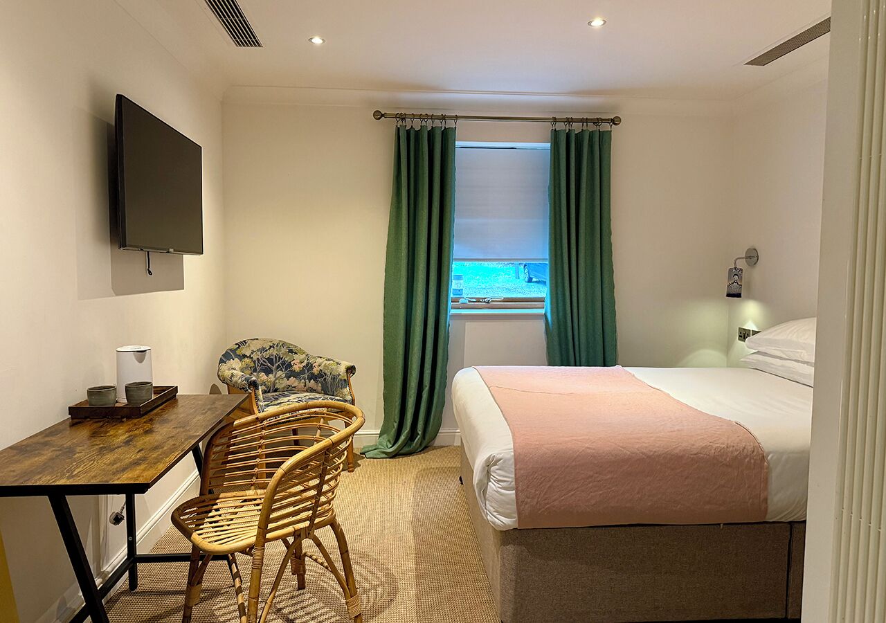 Una habitación de hotel con cama, escritorio, silla, televisor y ventana con cortinas.