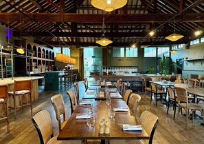 Un restaurant avec des tables et des chaises en bois, un coin bar et de grandes fenêtres.