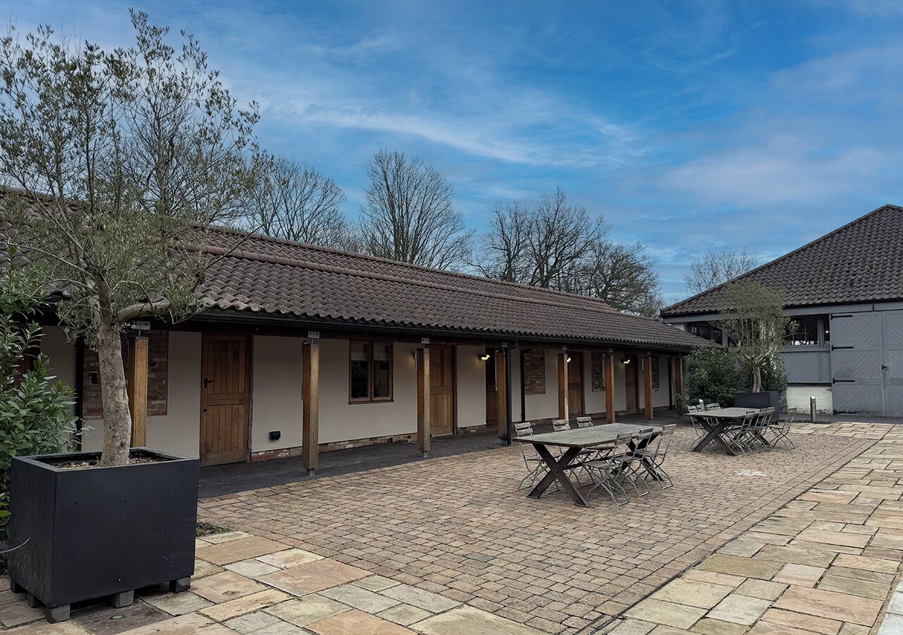 A building with a tiled roof, a covered patio area with tables and chairs, and a large planter box.