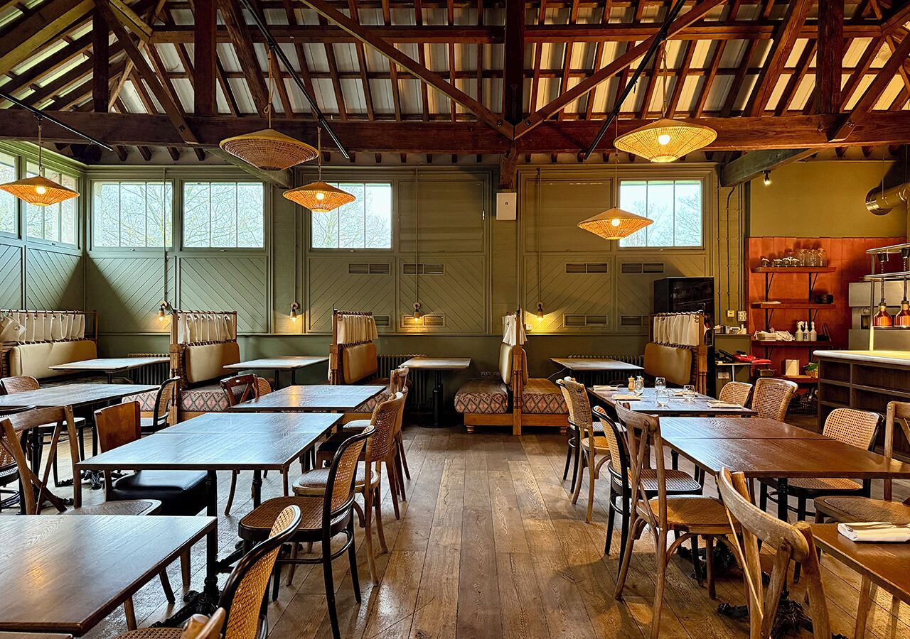 Un comedor amplio con mesas y sillas de madera, ventanas grandes y lámparas de mimbre colgantes.