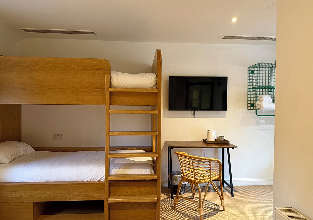 A bunk bed with a desk and chair, a television, and a green wire basket on the wall.