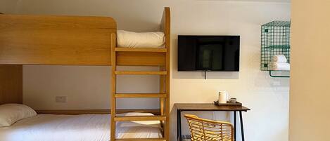A bunk bed with a desk and chair, a television, and a green wire basket on the wall.