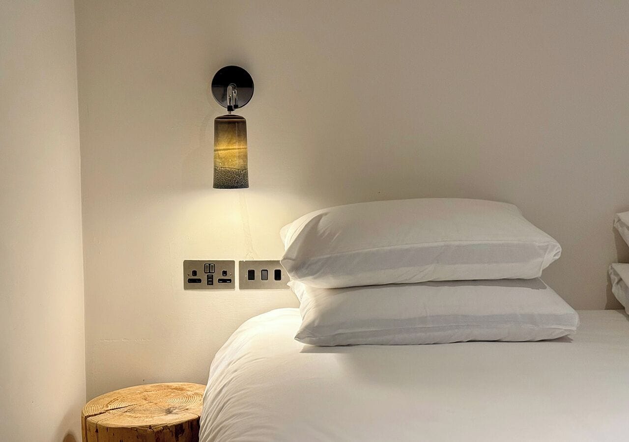 Un lit bien fait, avec du linge de lit blanc, et un luminaire fixé au mur.