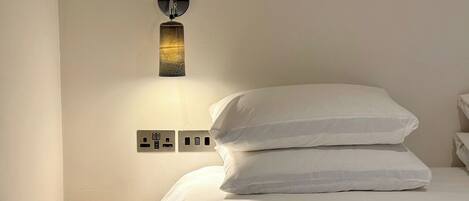 Un lit bien fait, avec du linge de lit blanc, et un luminaire fixé au mur.