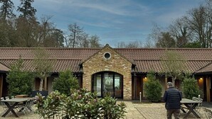 Een gebouw van baksteen met een pannendak en een centrale ingang. Er staan buiten tafels en stoelen voor.
