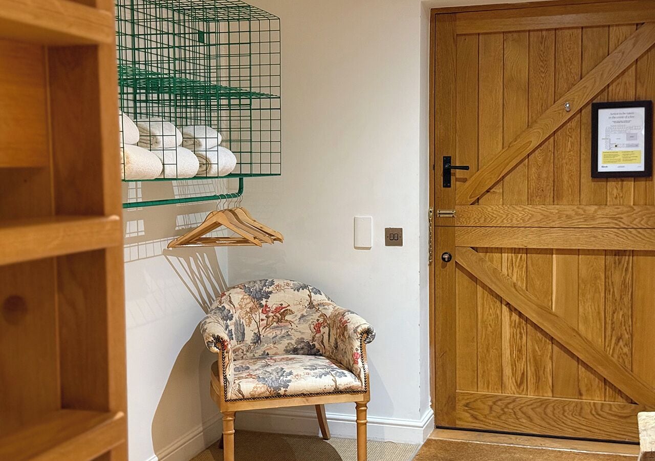 A wooden door with a metal gate, a floral armchair, and a green metal rack with towels.